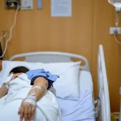Pacjentka w szpitalnym łóżku, podłączona do kroplówki, walczy z chorobą, która przypomina dżumę.
