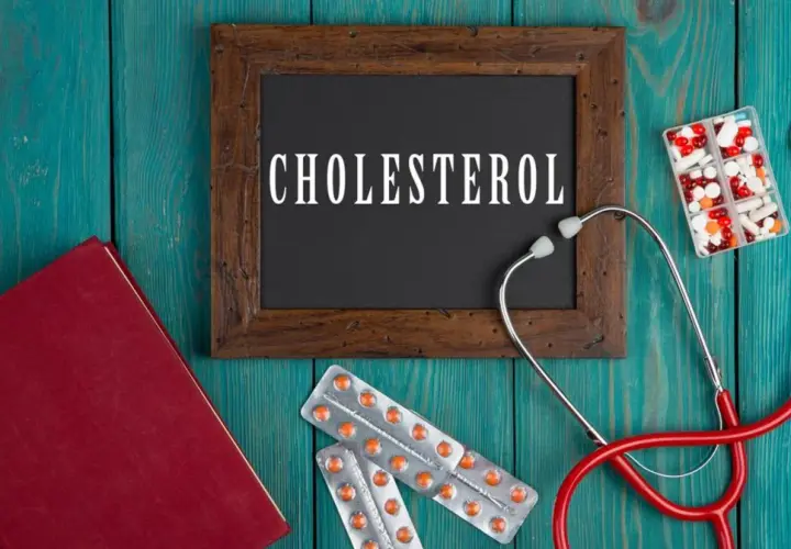 Lekarz bada cholesterol. Na drewnianym tle leżą stetoskop, książka, tabletki i opakowania leków, w tym Lipanthyl.