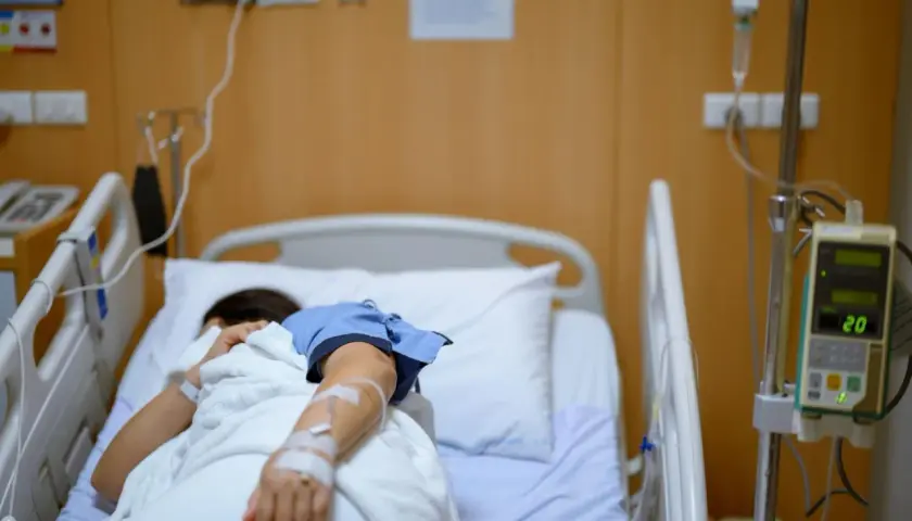 Pacjentka w szpitalnym łóżku, podłączona do kroplówki, walczy z chorobą, która przypomina dżumę.