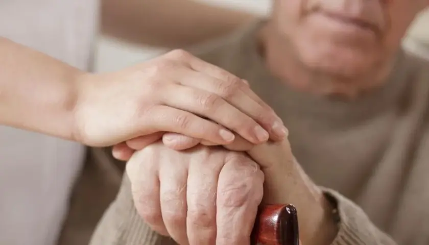 Dłoń opiekunki na dłoni starszego mężczyzny, który trzyma laskę. Wsparcie i troska, jak przy leczeniu chorób, np. parkinsonizmu, gdzie pomocne bywa Madopar.
