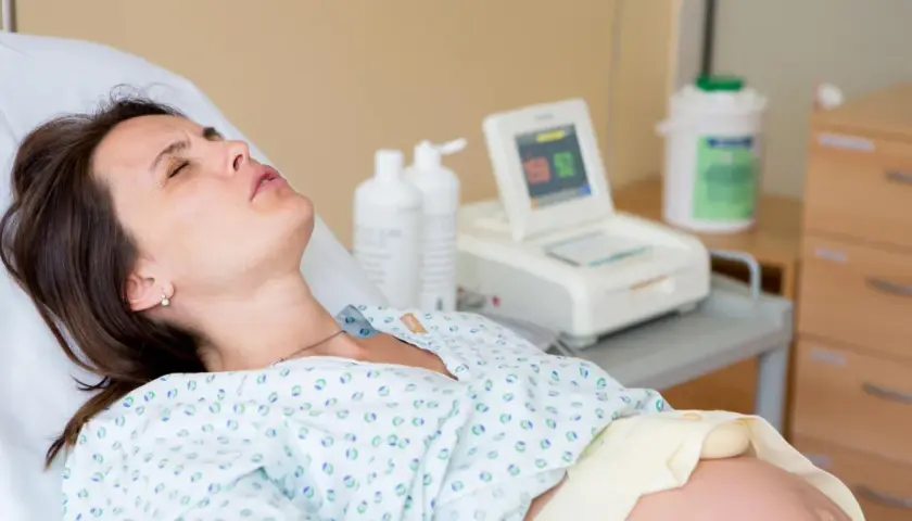 Kobieta w szpitalnym łóżku, monitor KTG, butelki z płynem. Badanie może wykluczyć obecność bakterii Streptococcus agalactiae.