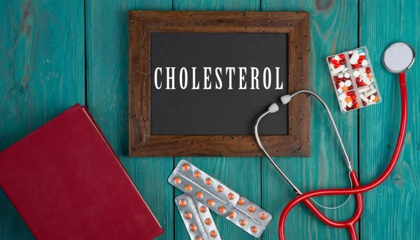 Lekarz bada cholesterol. Na drewnianym tle leżą stetoskop, książka, tabletki i opakowania leków, w tym Lipanthyl.