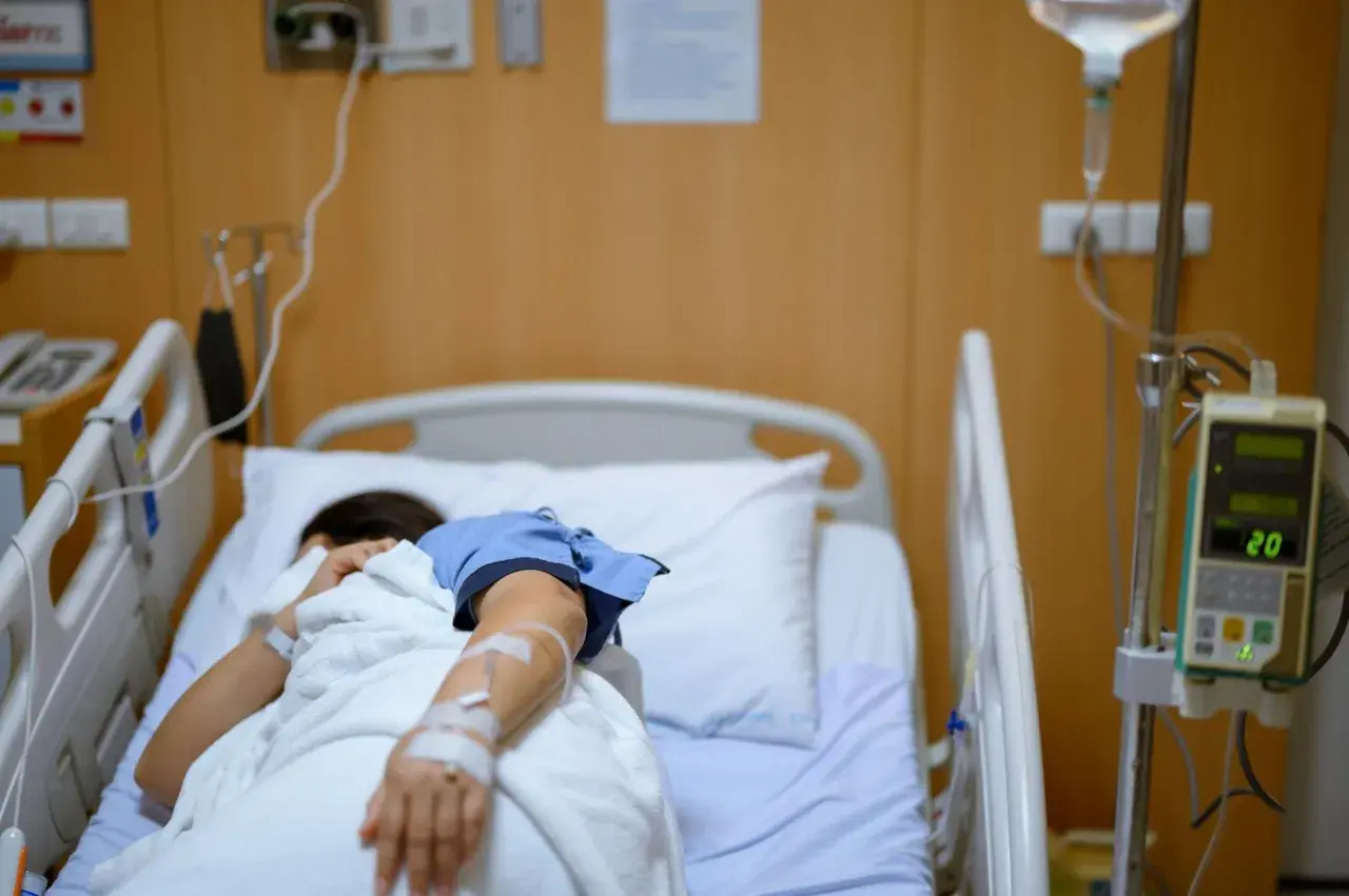 Pacjentka w szpitalnym łóżku, podłączona do kroplówki, walczy z chorobą, która przypomina dżumę.